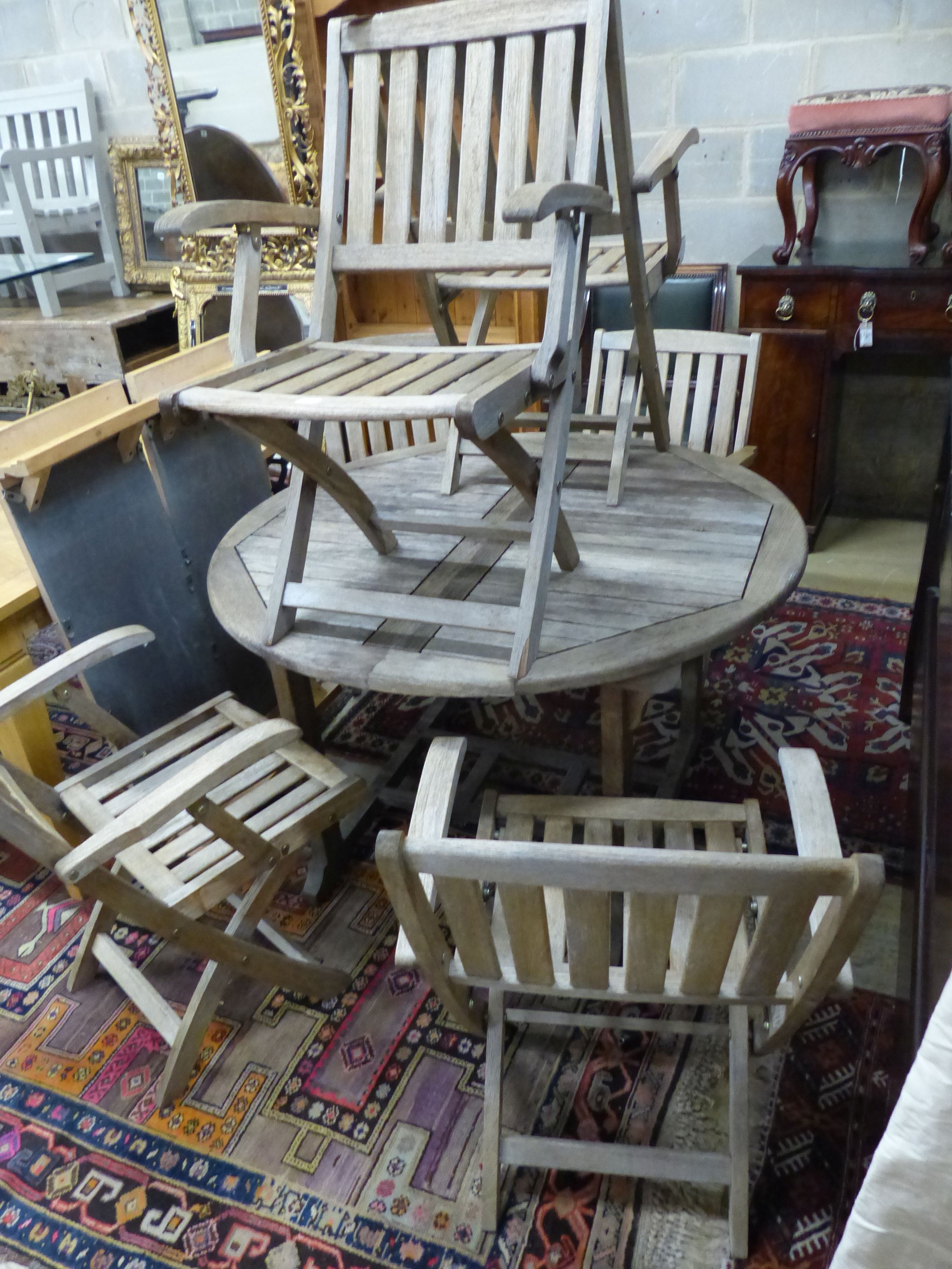 A circular weathered teak extending garden table, 180cm extended, W.120cm H.70cm and six folding garden armchairs